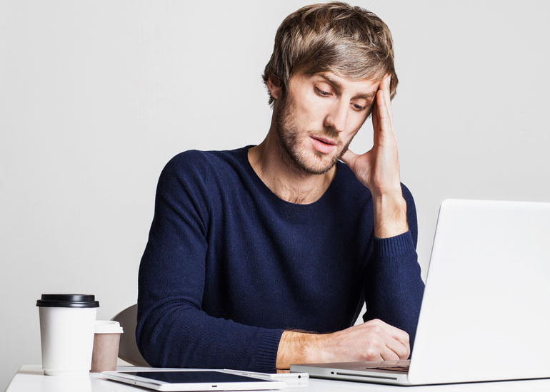 Stressed man sitting at laptop with coffee