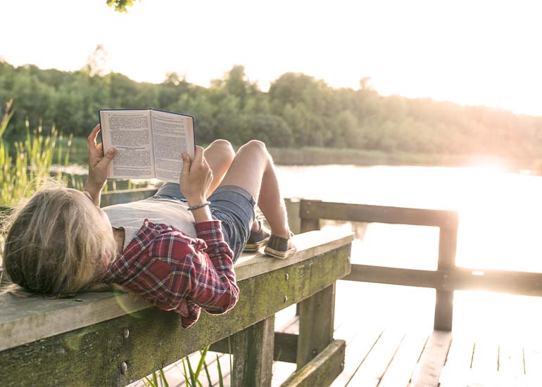 woman lying on dock by a lake reading a book