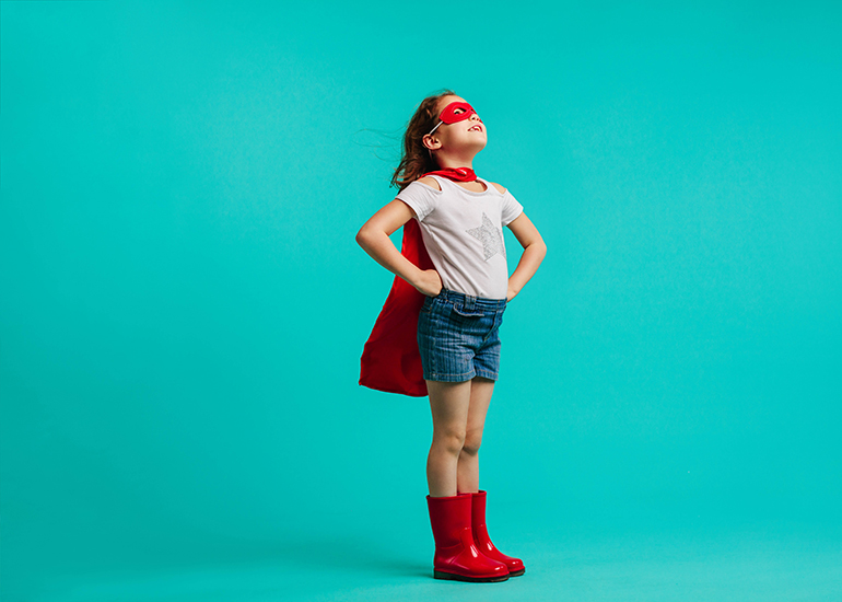 Confident little girl in cape, eye mask, and gumboots