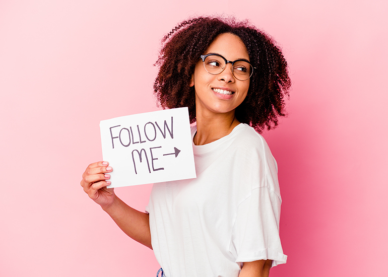 Young woman holding sign which reads 'follow me'