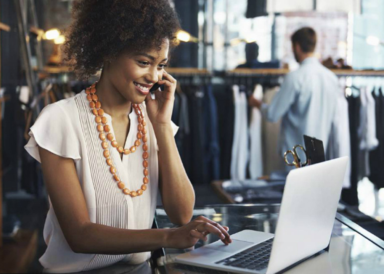 Woman using laptop device in store with customer in background