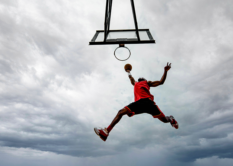 man leaping high to dunk a basketball through hoop
