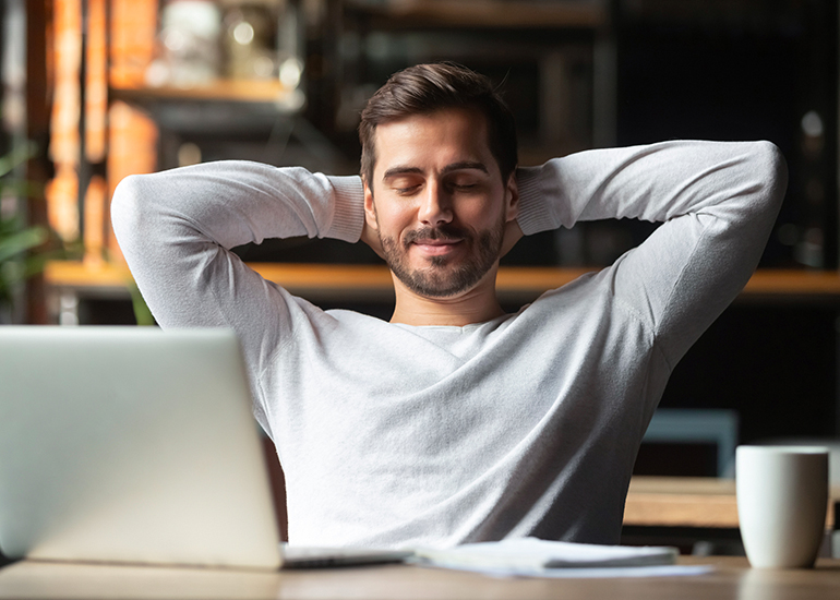 Man looking content sitting at desk with hands behind head