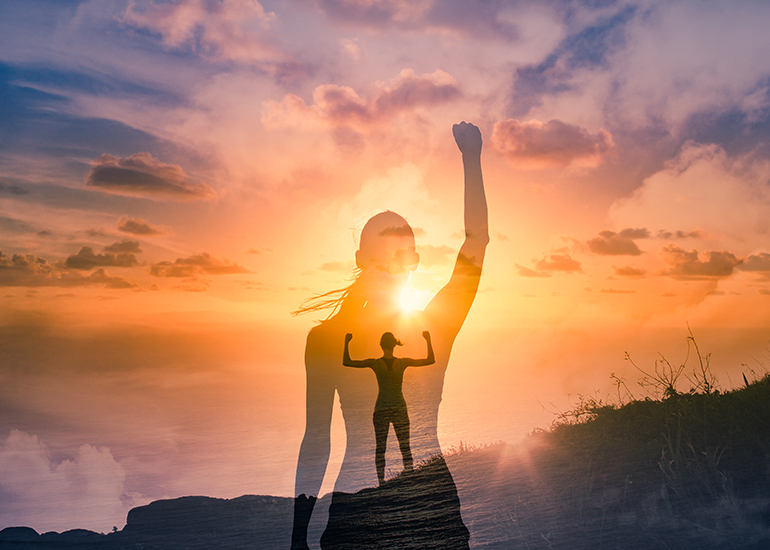 Fit, strong woman on mountain top with arms raised in victory