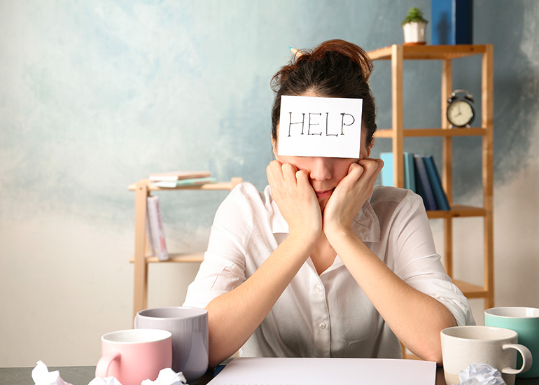 Stressed woman at desk with 'help' sign on her forehead