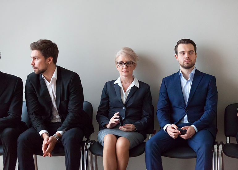 mature-aged woman sitting with younger candidates in job interview lineup