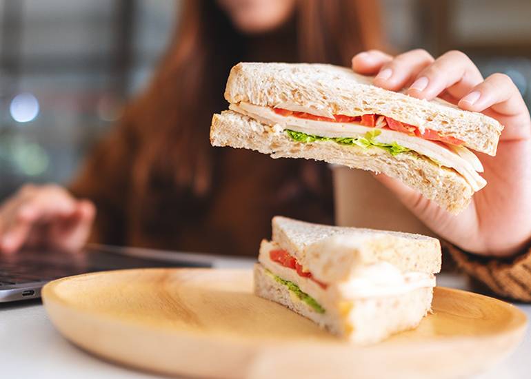 Woman holding sandwich while working at desk