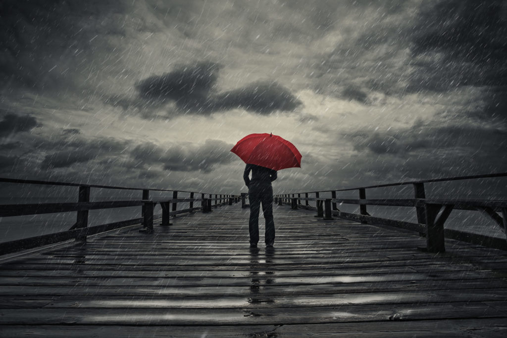 Person standing with red umbrella on pier in storm weather