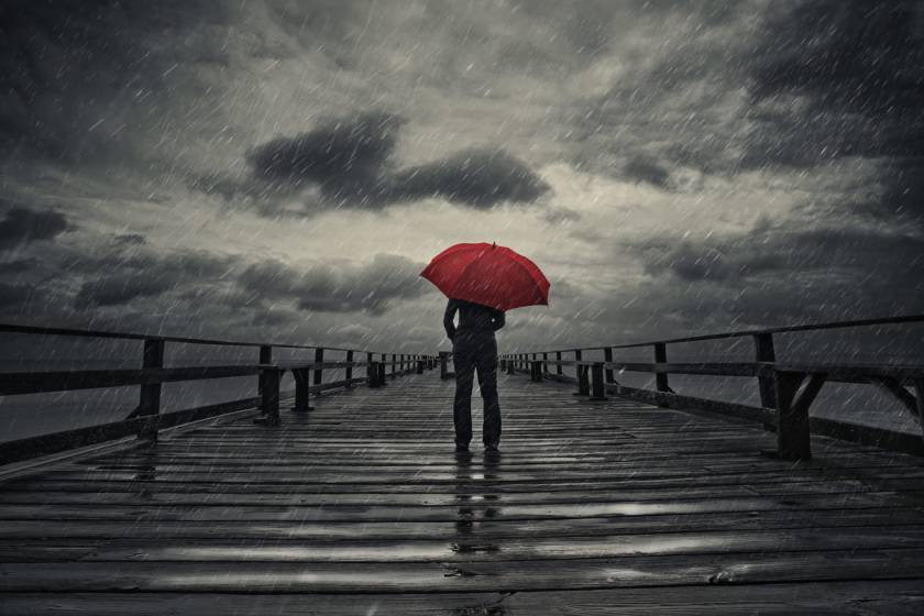 Person standing with red umbrella on pier in storm weather