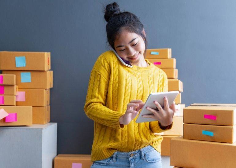 Woman working with mobile phone and tablet with cardboard boxes