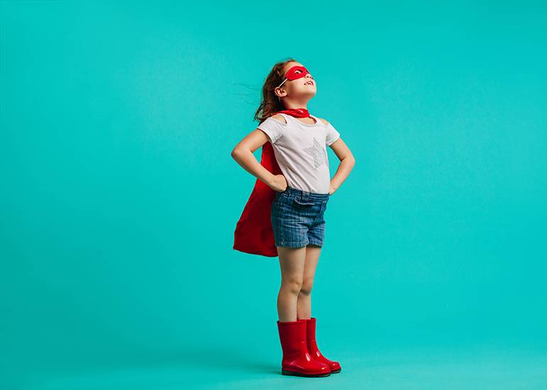 Confident little girl in cape, eye mask, and gumboots