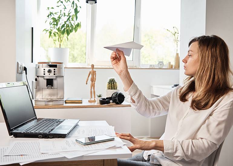 Woman procrastinating at desk with paper plane
