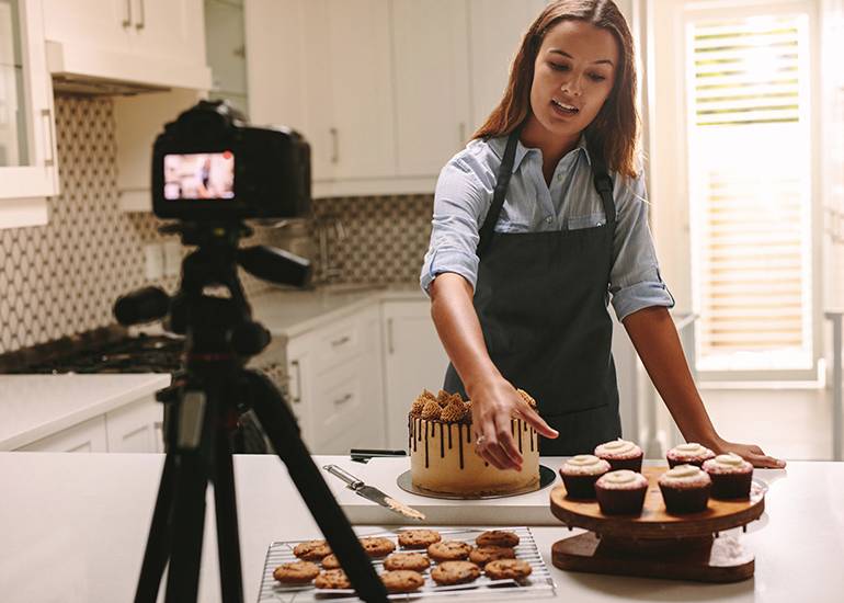 Young female baker creating social media video while baking cake