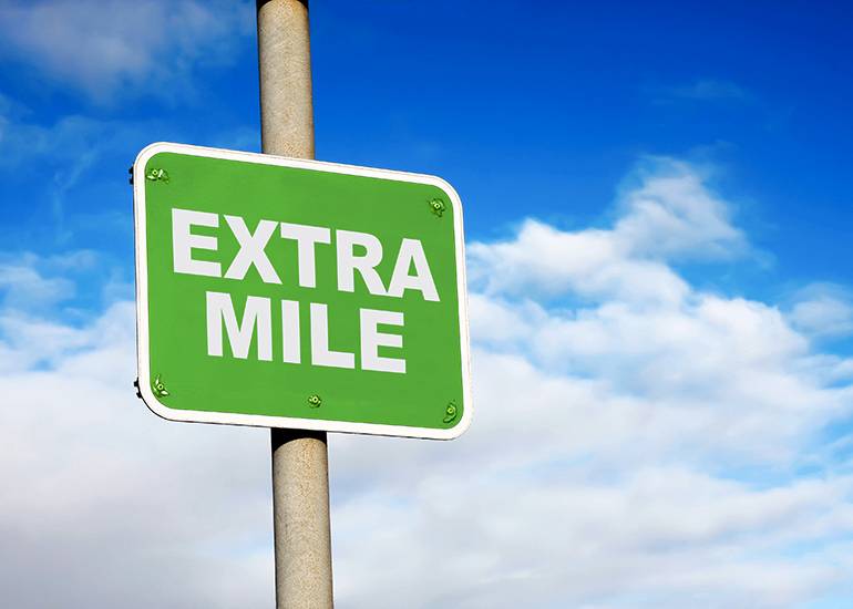 Green extra mile signpost against a blue sky backdrop