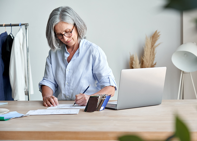 Mature aged business woman working at desk with notepad and laptop