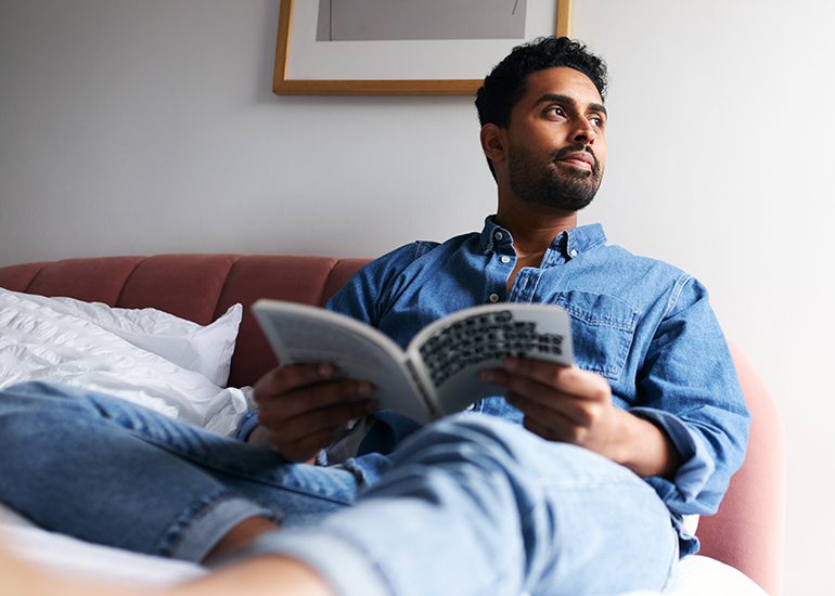 Young man relaxing on bed at home reading book