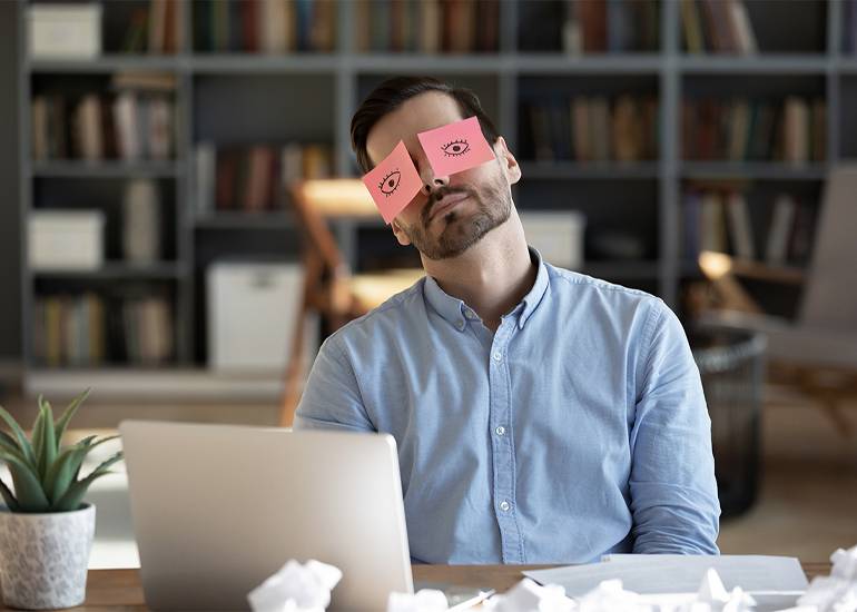 Tired man at desk with post-it notes with eyes stuck on his own eyes