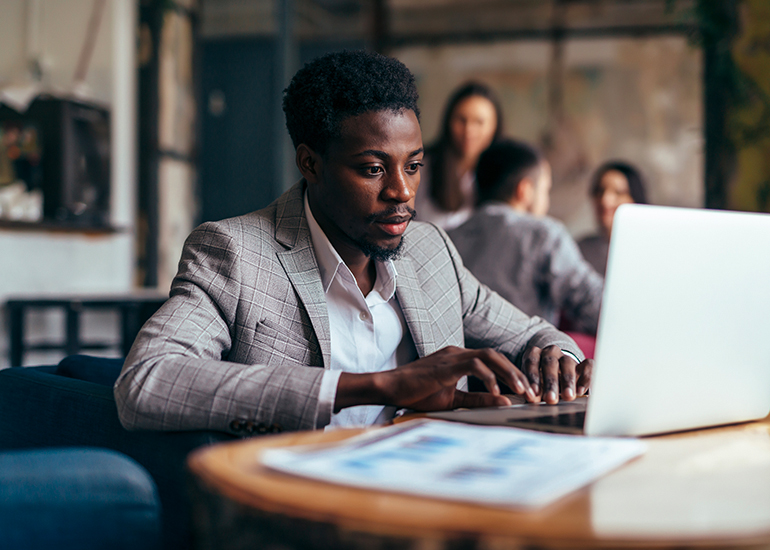 Man in business suit working on laptop in cafe or crowded space