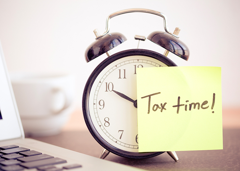 Old fashioned alarm clock with post-it note attached reading ‘tax time’