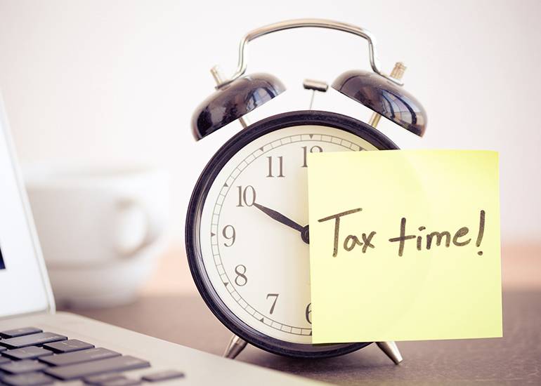 Old fashioned alarm clock with post-it note attached reading ‘tax time’