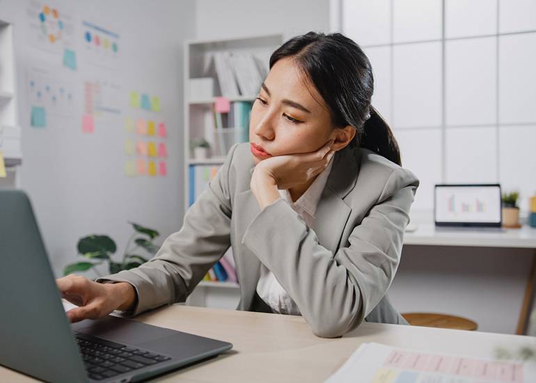 Bored, tired woman slumping at desk while scrolling on laptop