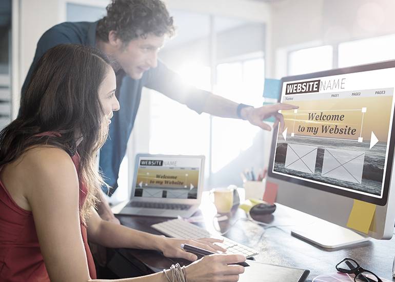 Two people looking at computer screen as they build a website