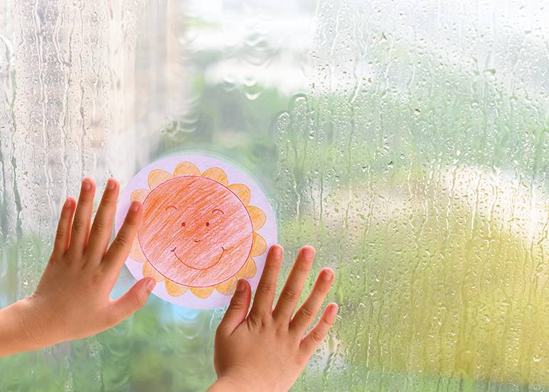 child's hands sticking a sunshine drawing onto a rainy window pane