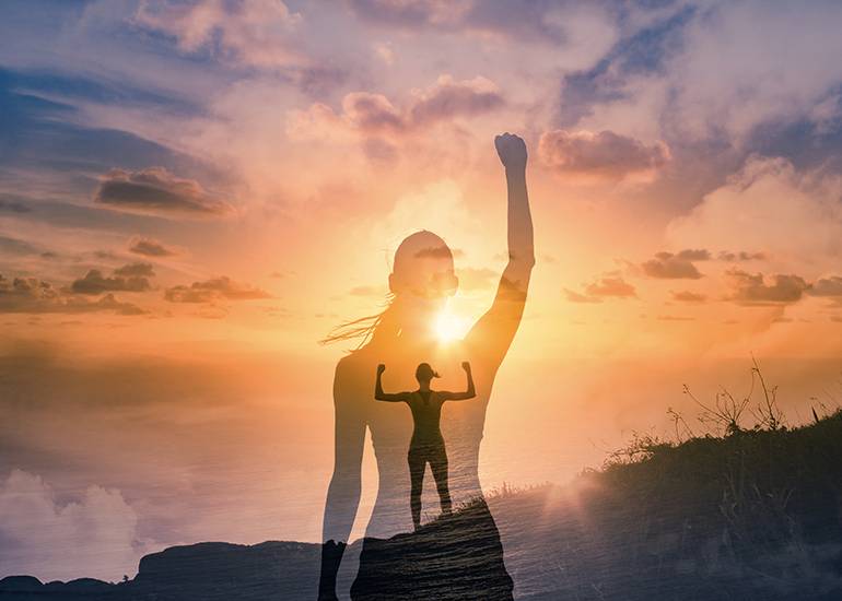 Fit, strong woman on mountain top with arms raised in victory