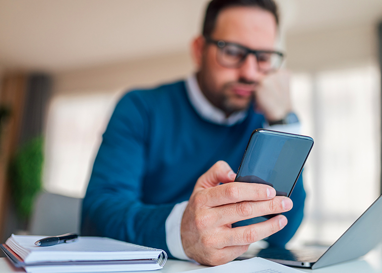 Bored man using smartphone at office desk