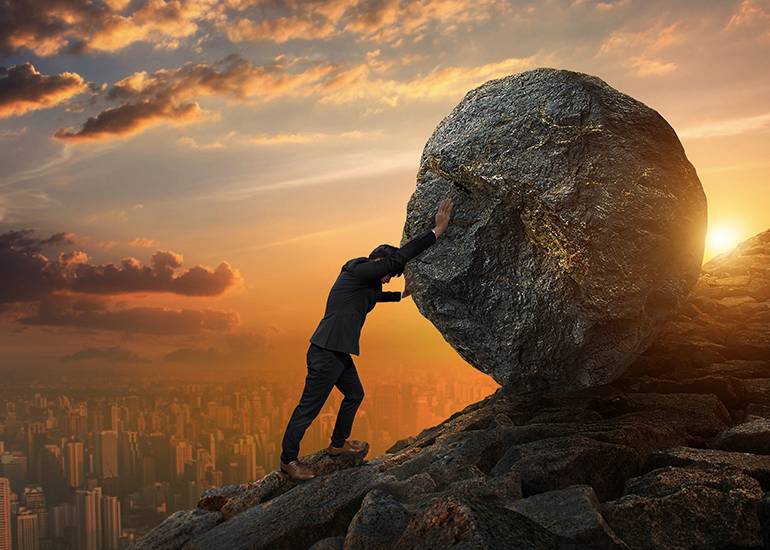 Business man pushing large boulder up a hill
