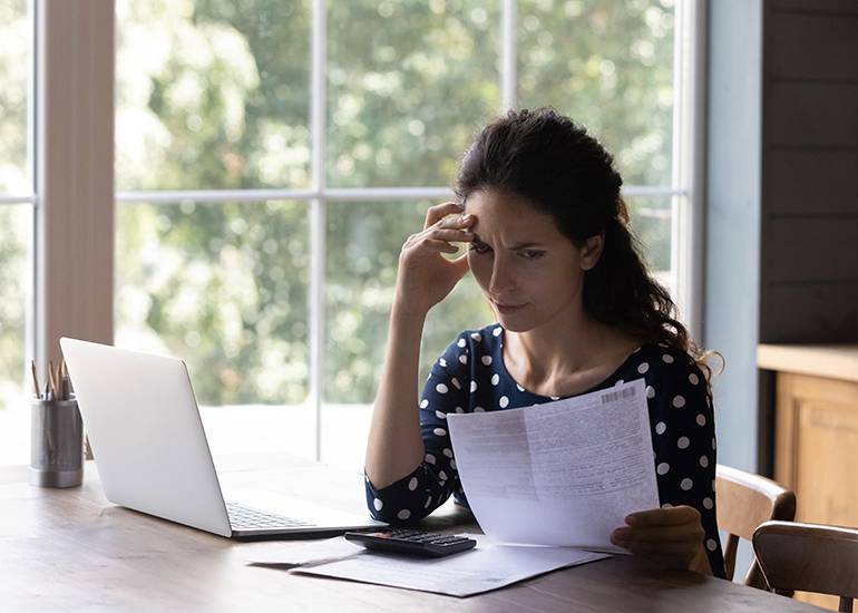 woman at table looking worriedly at bills and invoices