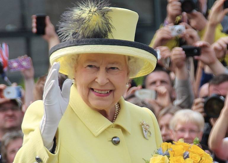 Queen Elizabeth II in yellow suit and hat, waving to crowds
