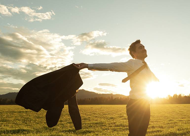 Happy man outdoors with arms spread wide and suit coat in his hand