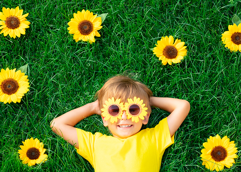 happy, smiling young boy lying in the grass with sunflowers