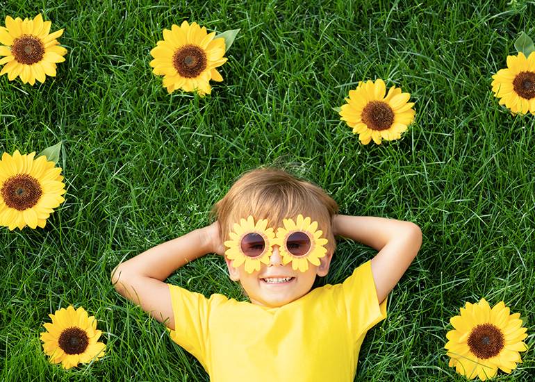 happy, smiling young boy lying in the grass with sunflowers