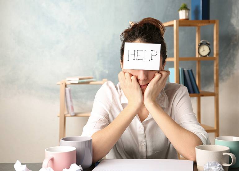 Stressed woman at desk with 'help' sign on her forehead