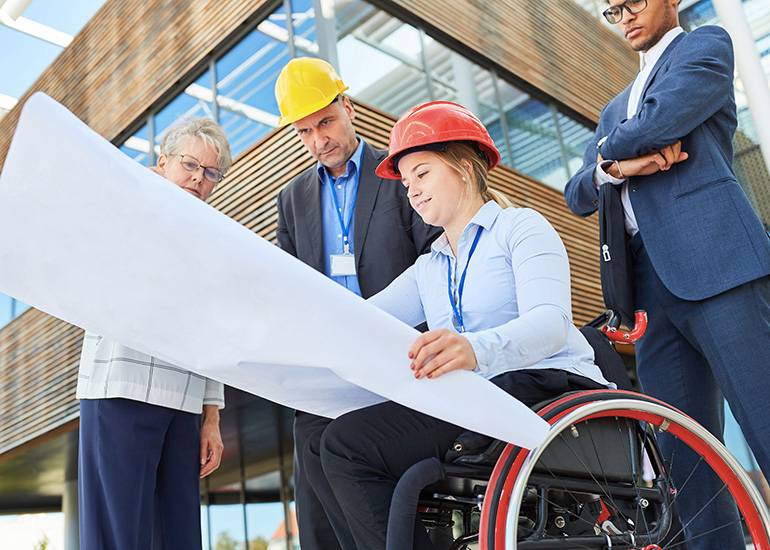 Young woman in wheelchair showing colleagues an architecture blueprint