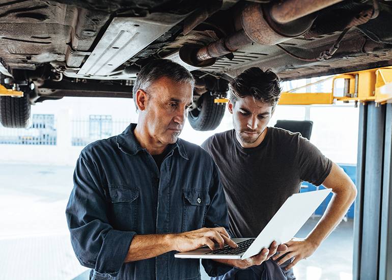 Mature tradie mechanic using laptop under car