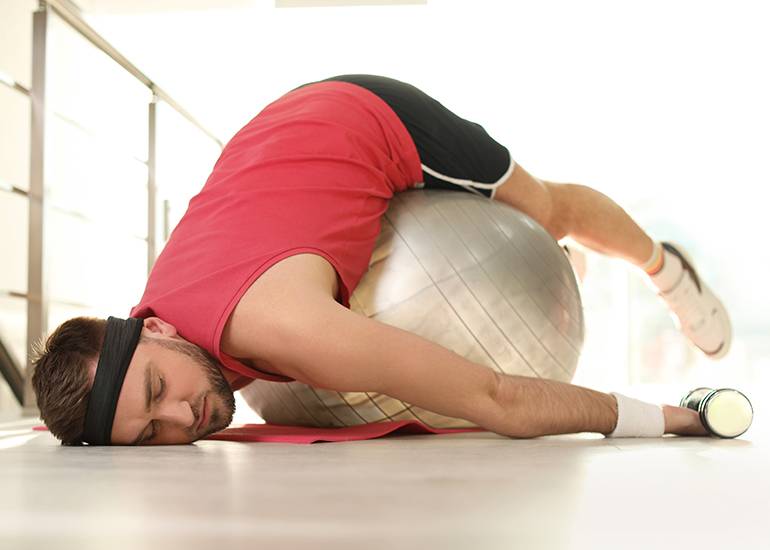 Man slumped exhausted over exercise yoga ball
