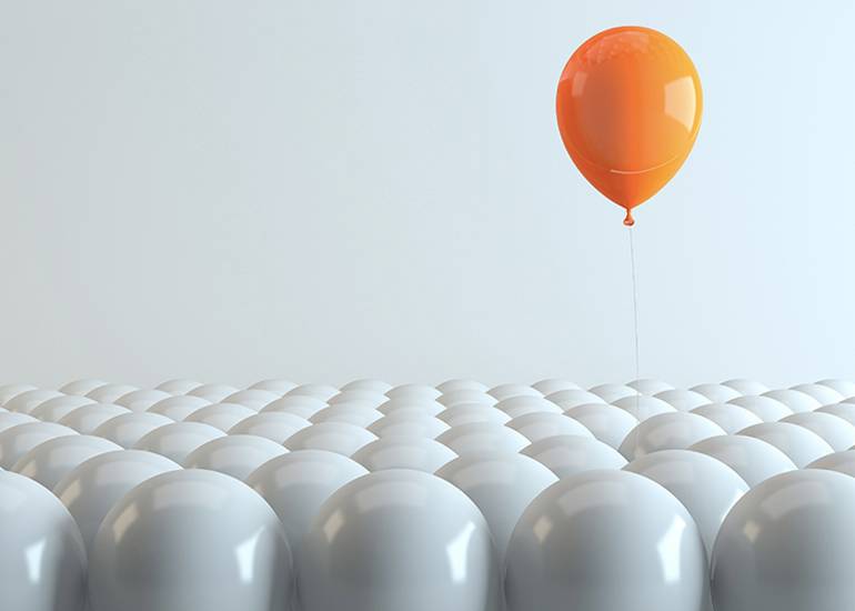 single orange balloon rising out of sea of white balloons