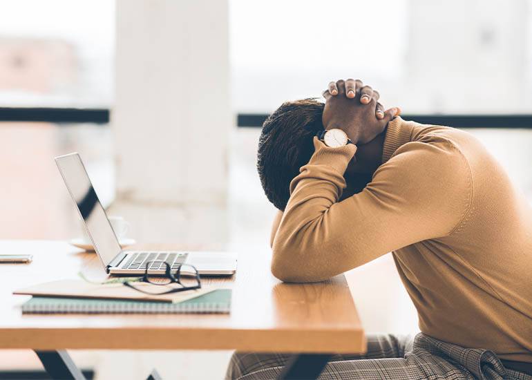 Tired, burnt out worker with head in hands at desk
