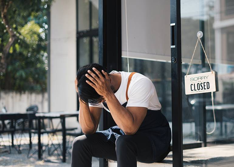 Depressed business owner with head in hands outside failed/closed restaurant