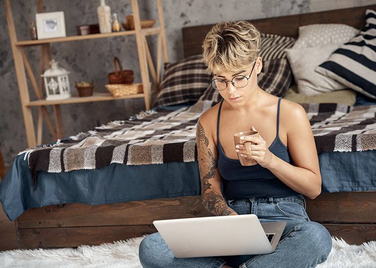 millennial on laptop in bedroom drinking coffee