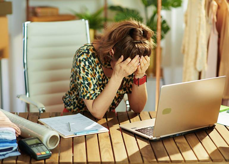 Stressed, exhausted woman with head in hands at desk