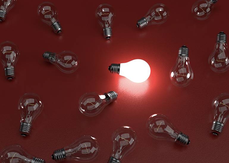 one lit lightbulb amongst other unlit bulbs