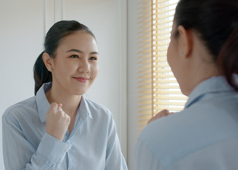 Happy woman giving herself a pep talk in a mirror