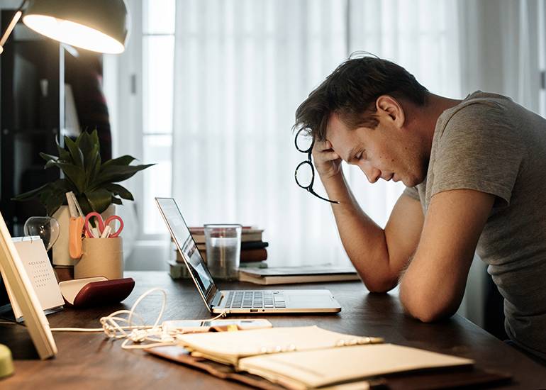 Man at home office desk with head in hands