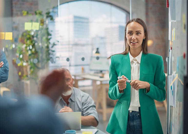 a woman stands at the front of a room pitching her business idea to investors