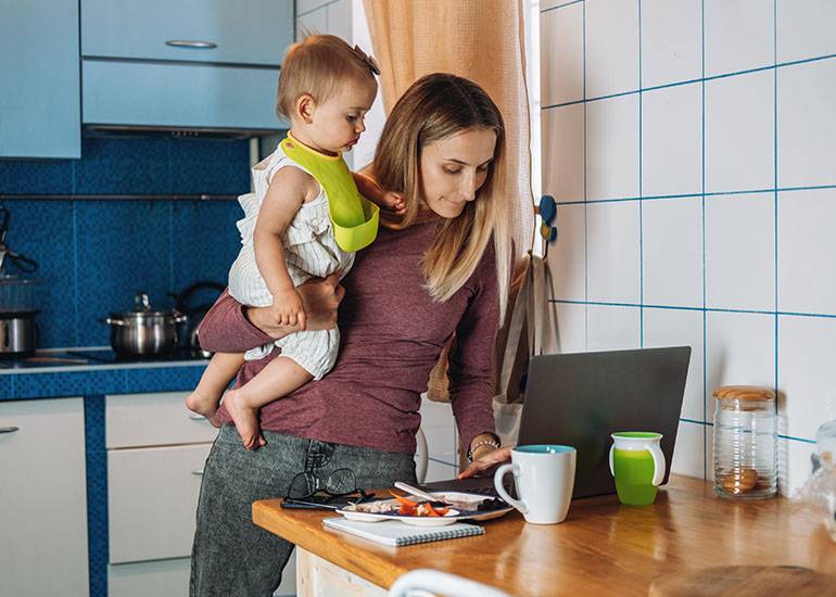 a mum juggles her toddler child and working on a computer: time poor concept
