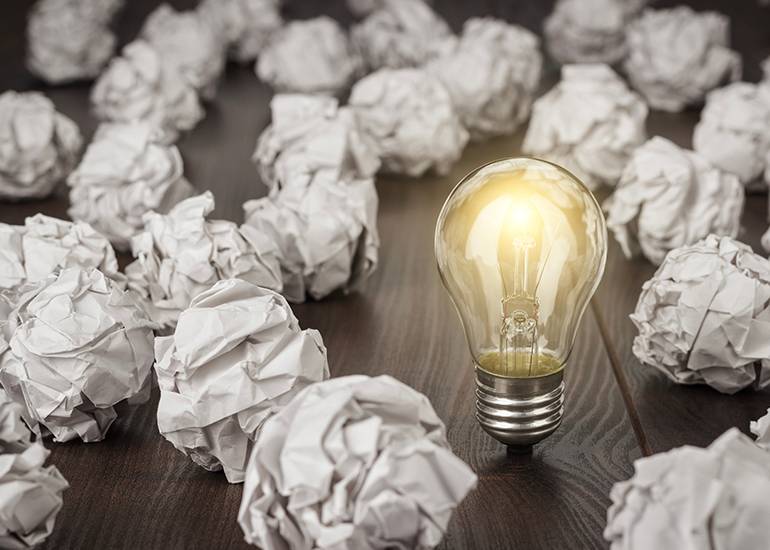 it's always important to validate your business ideas. Image of floor w covered in scrunched up paper balls in the midst of the paper is a lightglobe that is illuminated.